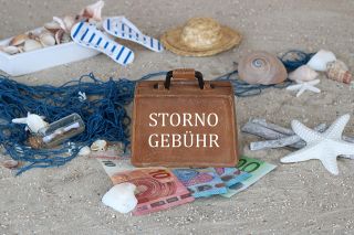 Foto: Sand, Muscheln, Geldscheine und Koffer mit Aufschrift Stornogebühr
